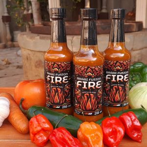 Three SPICY BLAZE bottles with bell peppers, onions, carrots, garlic, and Habanero Peppers on a table