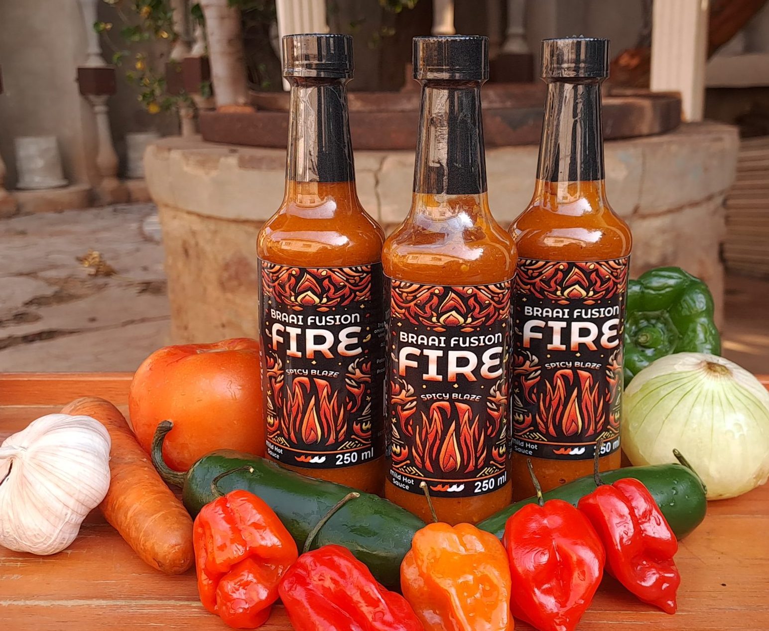 Three SPICY BLAZE bottles with bell peppers, onions, carrots, garlic, and Habanero Peppers on a table